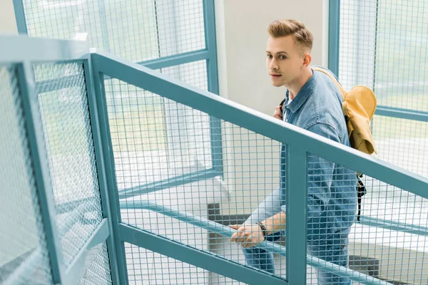 Estudiante en camisa de mezclilla con mochila amarilla en las escaleras en la universidad - foto de stock