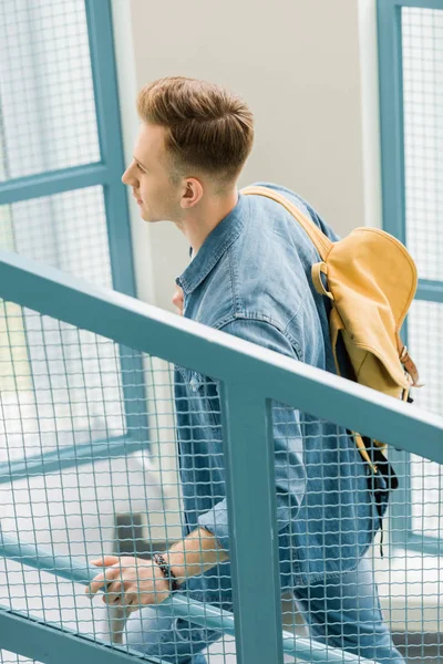Estudante em camisa jeans com mochila amarela em escadas na universidade — Fotografia de Stock