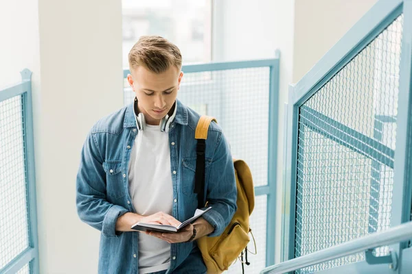 Concentrated student in denim shirt and headphones with yellow backpack in university — Stock Photo