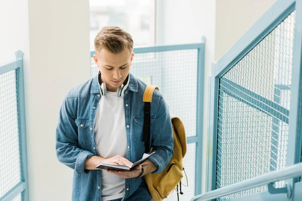 Studente concentrato in camicia denim e cuffie con zaino giallo all'università — Foto stock