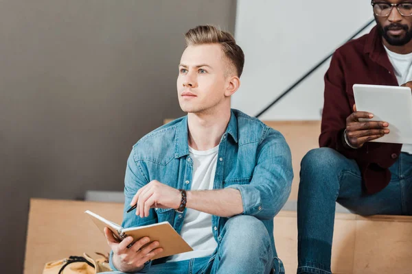 Zwei multiethnische Studenten mit Notizbuch und digitalem Tablet im Hörsaal — Stockfoto