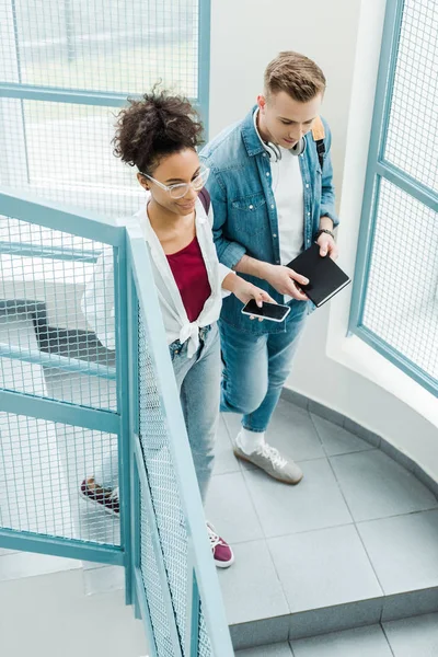 Overhead view of two students with notebook and smartphone standing on stairs — Stock Photo