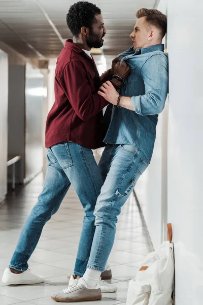 Full length view of two students in jeans fighting in corridor in college — Stock Photo