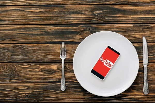 Top view of smartphone with youtube app on screen on brown wooden surface near knife and fork — Stock Photo