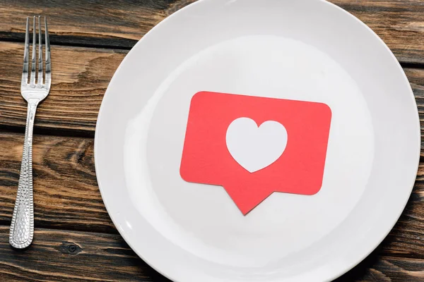 Red paper cut card with heart symbol near fork on brown wooden surface — Stock Photo