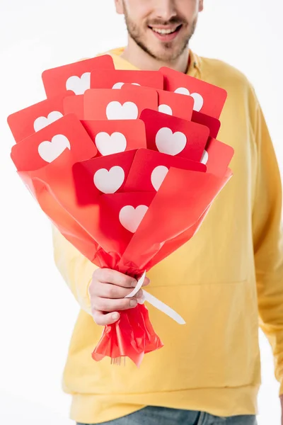 Vue recadrée d'un homme souriant tenant un bouquet de carton rouge avec des symboles de coeur isolés sur du blanc — Photo de stock