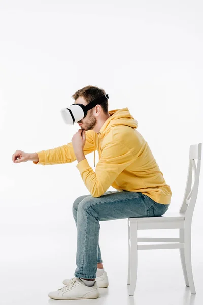 Jeune homme en réalité virtuelle casque imitant l'écriture tout en étant assis sur une chaise sur fond blanc — Photo de stock