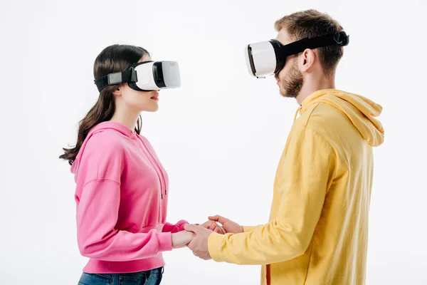 Young man and woman holding hands while using virtual reality headsets isolated on white — Stock Photo