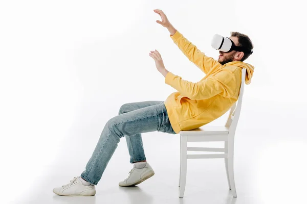 Junger Mann mit ausgestreckten Händen sitzt auf Stuhl in Virtual-Reality-Headset auf weißem Hintergrund — Stockfoto