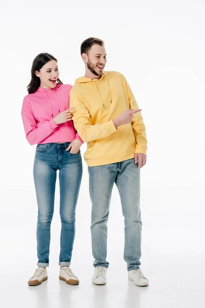 Молодые улыбающиеся мужчина и женщина в толстовках и синих джинсах указывая пальцами на белом фоне — стоковое фото