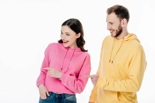 Joven alegre hombre y mujer en sudaderas con capucha señalando con los dedos y mirando hacia otro lado aislado en blanco - foto de stock