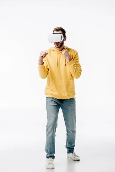 Junger Mann in blauen Jeans und gelbem Kapuzenpullover imitiert Boxen, während er Virtual-Reality-Headset auf weißem Hintergrund benutzt — Stockfoto