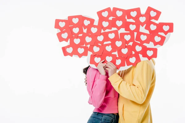 Joven hombre y mujer en sudaderas con capucha brillante escondido detrás de caras detrás de tarjetas de papel rojo cortadas con símbolos del corazón aislados en blanco - foto de stock