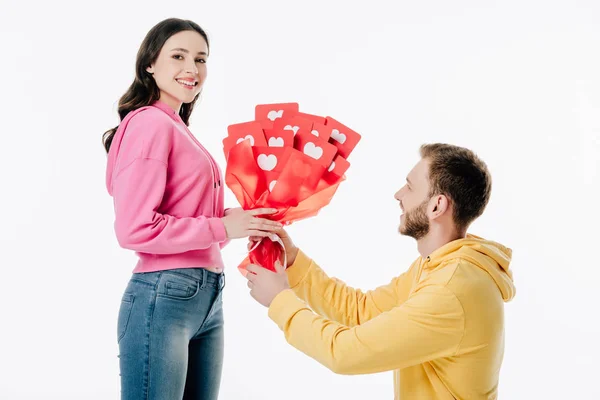 Bel giovane uomo regalo bouquet di carte tagliate di carta rossa con i simboli del cuore alla bella ragazza isolata su bianco — Foto stock