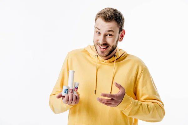 Jeune homme excité en sweat à capuche jaune tenant des conteneurs avec des logos de médias sociaux isolés sur blanc — Photo de stock