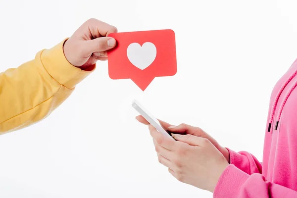 Vue recadrée de l'homme tenant carte de coupe de papier rouge avec symbole de coeur et femme en utilisant smartphone isolé sur blanc — Photo de stock