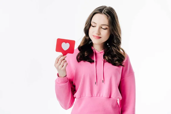 Bonita joven en sudadera con capucha rosa con tarjeta de corte de papel rojo con símbolo del corazón aislado en blanco - foto de stock