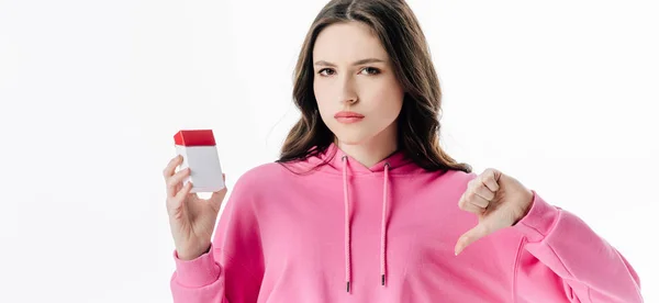 Panoramic shot of pretty serious girl holding cigarette pack and showing thumb down isolated on white — Stock Photo