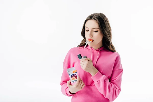 Menina bonita com cigarros na boca segurando maço de cigarro com logotipo instagram isolado no branco — Fotografia de Stock