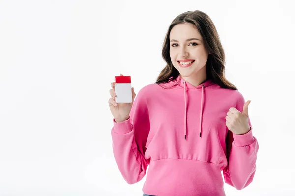 Alegre chica joven sosteniendo paquete de cigarrillos y mostrando el pulgar hacia arriba aislado en blanco - foto de stock