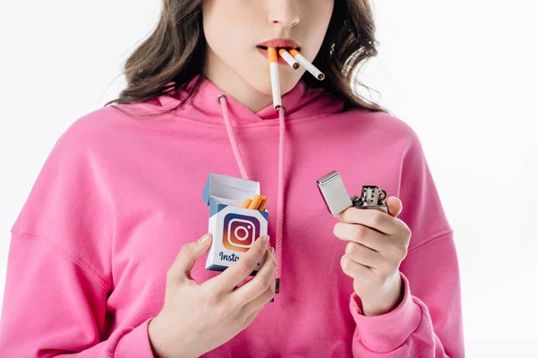 Vue recadrée de la jeune fille avec des cigarettes dans la bouche tenant paquet de cigarettes avec logo instagram isolé sur blanc — Photo de stock