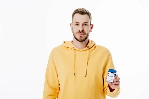 Schöner junger Mann in gelbem Kapuzenpullover mit Zigarettenschachtel und Facebook-Logo auf weißem Hintergrund — Stockfoto