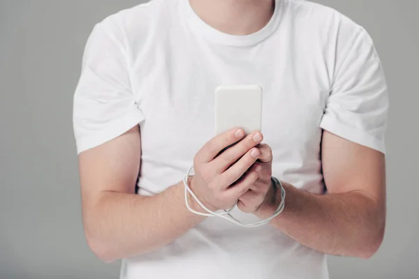 Vue partielle du jeune homme avec câble USB autour des mains à l'aide d'un smartphone isolé sur gris — Photo de stock