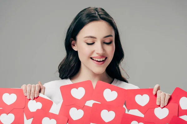 Bonita chica sonriente sosteniendo tarjetas de papel rojo cortadas con corazones símbolos aislados en gris - foto de stock