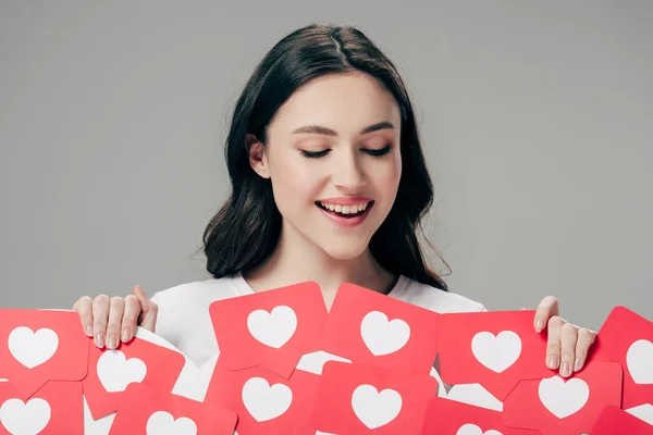 Pretty smiling girl holding red paper cut cards with hearts symbols isolated on grey — Stock Photo