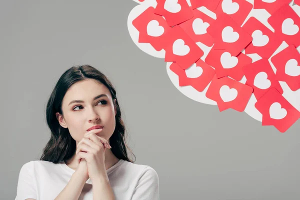 Jolie fille rêveuse regardant des cartes rouges coupées en papier avec des coeurs symbole isolé sur gris — Photo de stock