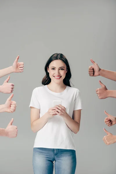 Cropped view of men and women showing thumbs up near happy girl with smartphone isolated on grey — Stock Photo
