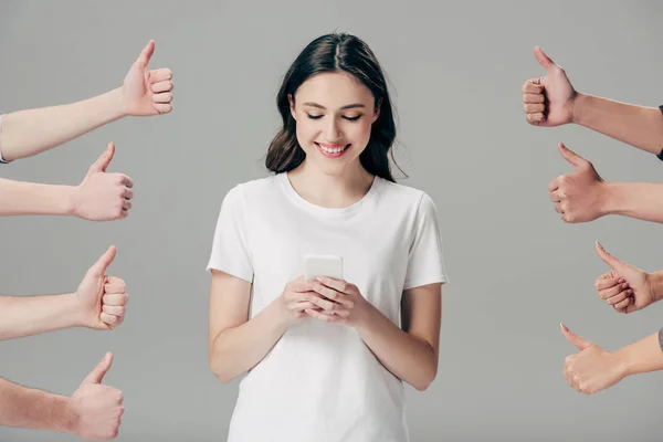 Partial view of men and women showing thumbs up near happy girl using smartphone isolated on grey — Stock Photo