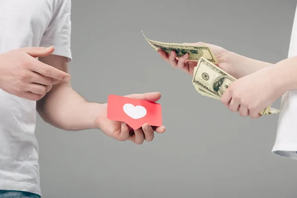 Vista recortada de mulher dando notas de dólar ao homem com cartão de corte de papel vermelho com símbolo de coração isolado em cinza — Fotografia de Stock