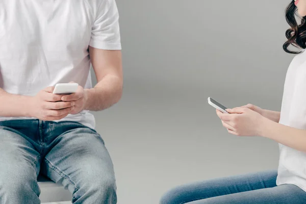 Vista recortada de hombre y mujer joven usando teléfonos inteligentes sobre fondo gris - foto de stock