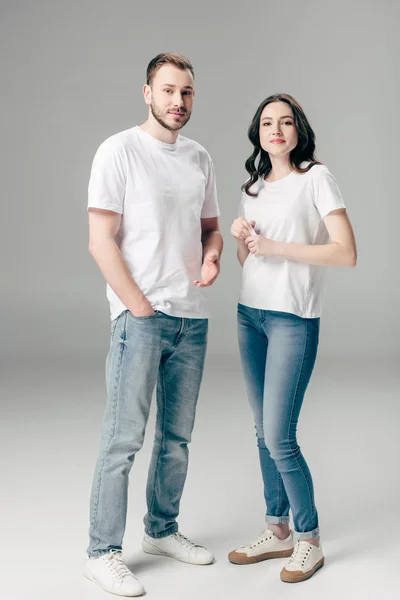 Jeune homme et femme en t-shirts blancs et jeans bleus regardant la caméra sur fond gris — Photo de stock