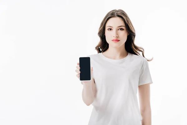 Chica confiada en camiseta blanca sosteniendo teléfono inteligente con pantalla en blanco y mirando a la cámara aislada en blanco - foto de stock