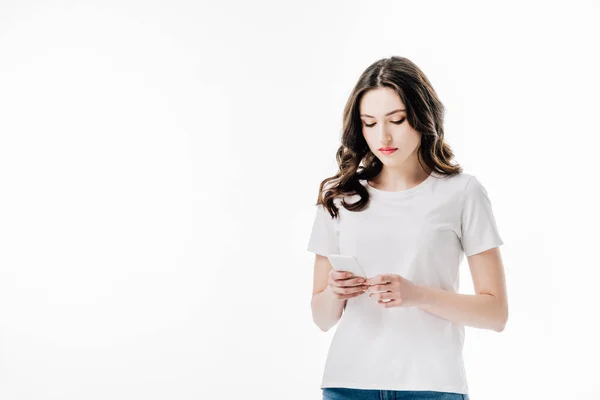 Концентрована молода жінка в білій футболці з використанням смартфона ізольована на білому — стокове фото