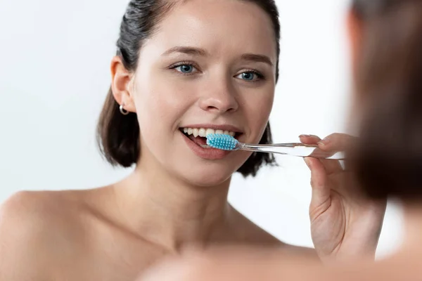 Alegre joven mujer cepillarse los dientes delante del espejo - foto de stock