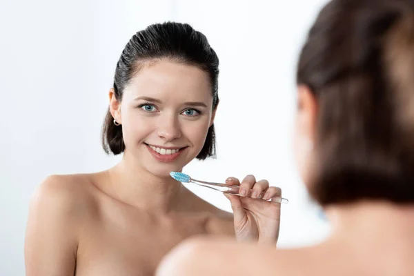 Досить усміхнена дівчина тримає зубну щітку біля дзеркала у ванній — стокове фото