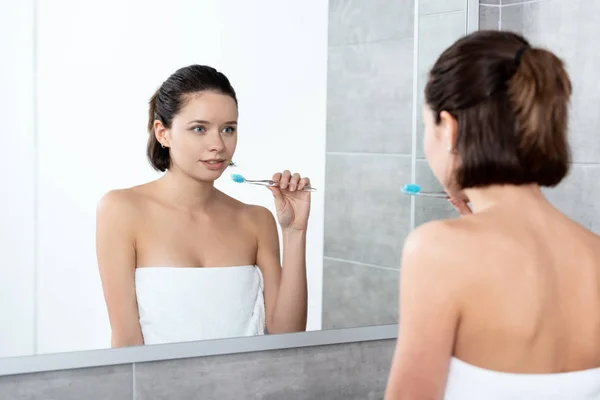 Mujer alegre en la toalla cepillarse los dientes delante del espejo - foto de stock