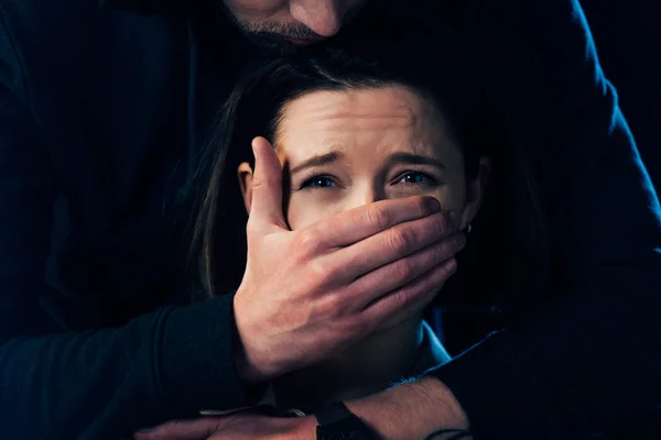 Частковий погляд на злочинця, який нападає на налякану жінку і прикриває рот ізольовано на чорному — стокове фото