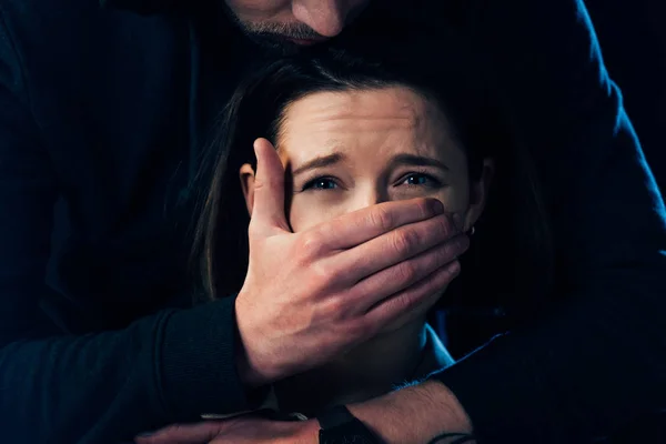 Partial view of criminal attacking scared woman and covering her mouth isolated on black — Stock Photo