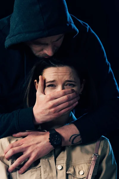 Partial view of criminal attacking scared woman and covering her mouth isolated on black — Stock Photo