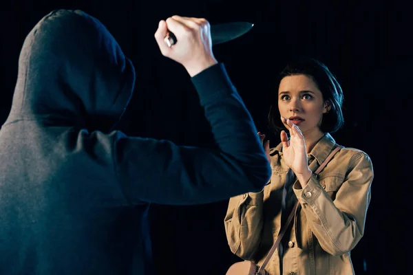 Partial view of criminal attacking woman with knife isolated on black — Stock Photo