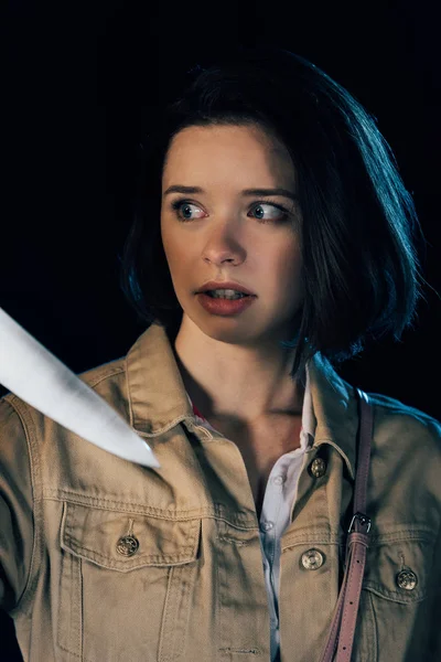 Pretty scared woman looking at knife isolated on black — Stock Photo