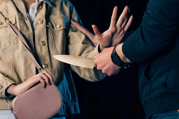 Partial view of criminal attacking woman with knife isolated on black — Stock Photo