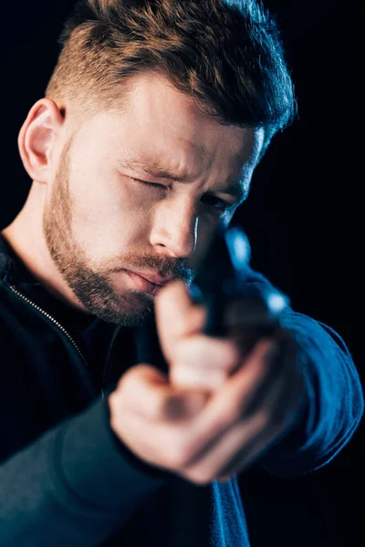 Criminel barbu visant pistolet à caméra isolé sur noir — Photo de stock