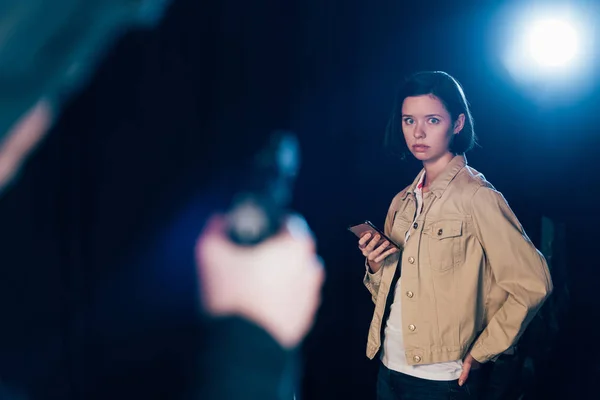 Cropped view of killer aiming gun at woman on black — Stock Photo