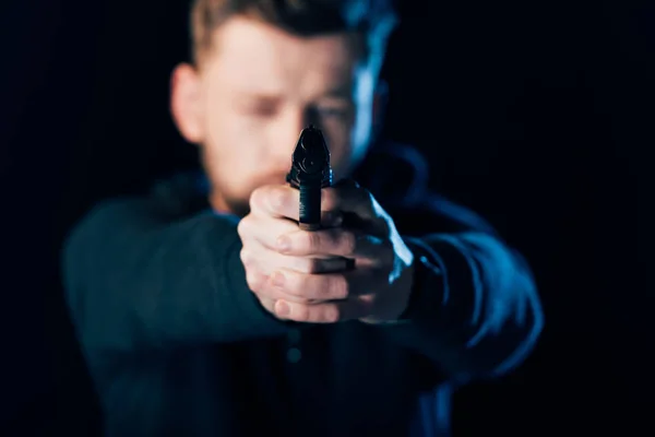 Selective focus of criminal aiming gun at camera isolated on black — Stock Photo