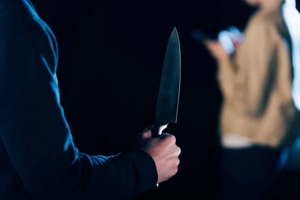 Обрізаний вид вбивці, що тримає ніж біля жінки ізольовано на чорному — стокове фото